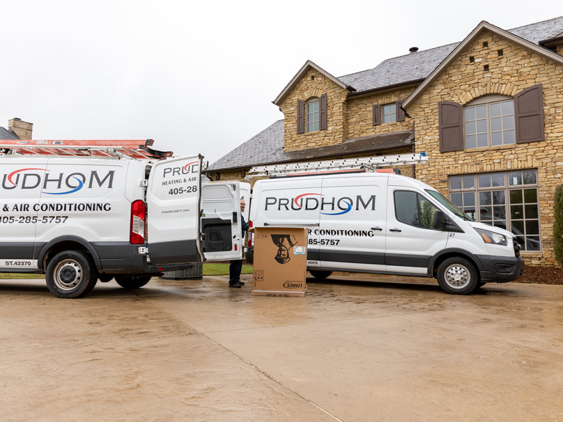 Prudhom vans unloading a Lennox AC outside a home